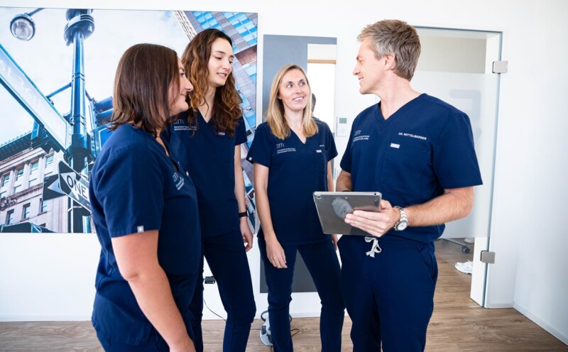 Das Team befindet sich in einer Besprechung. Dr. Mittelberger zeigt etwas auf seinem Tablet.