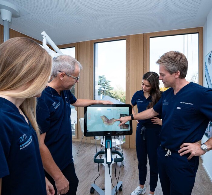 Das Team steht um einen Aufnahmescreen und unterh&auml;lt sich &uuml;ber das darauf abgebildete Zahnmodell.