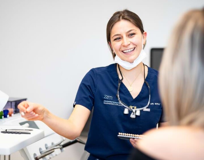 Eine Mitarbeiterin ber&auml;t anhand einer Zahnfarbskala eine Patientin.