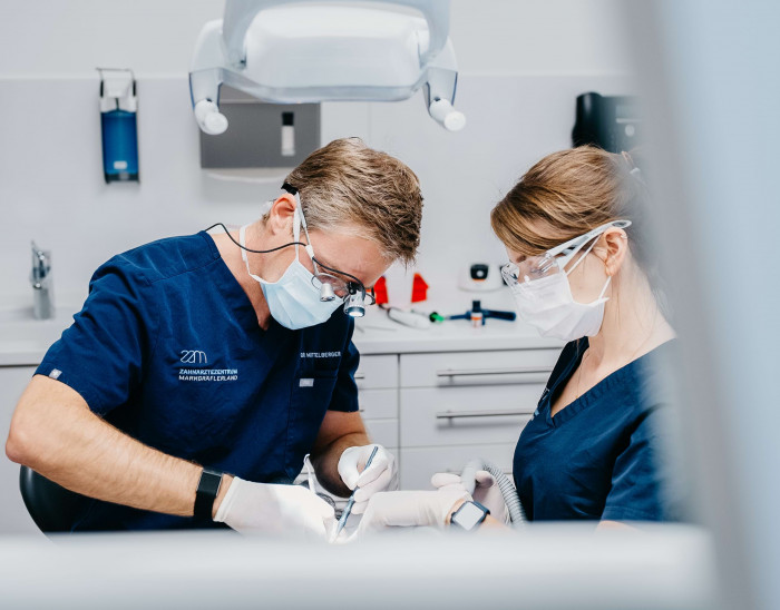 Dr. Mittelberger und eine Kollegin befinden sich in einer Behandlungssituation. Der Fokus ist auf dem Eingriff und die Patientin ist verdeckt.