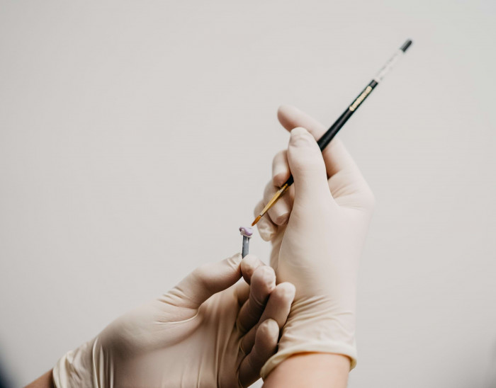 Ein Mini-Implantat wird mit feinem Werkzeug im Labor pr&auml;pariert.