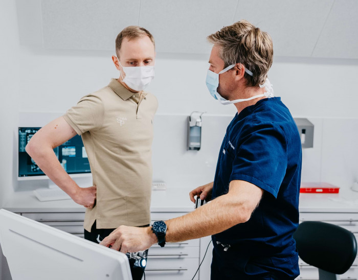 Dr. Mittelberger erkl&auml;rt einem Patienten etwas und zeigt dabei auf einen Bildschirm.