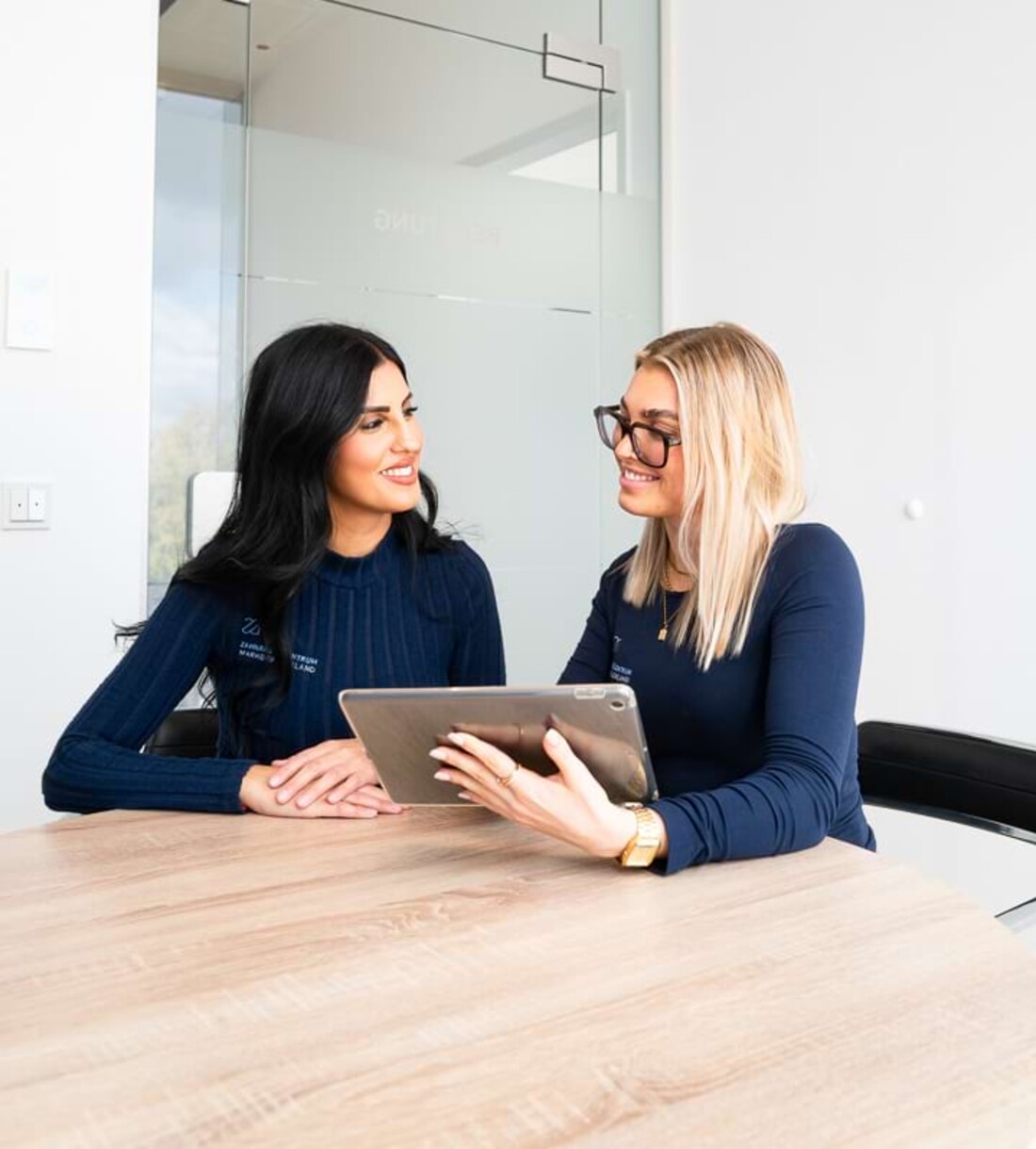 Zwei Mitarbeiterinnen unterhalten sich lachend und schauen gemeinsam auf ein Tablet.