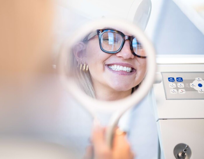 Nahaufnahme einer Patientin, die sich l&auml;chelnd im Handspiegel betrachtet.