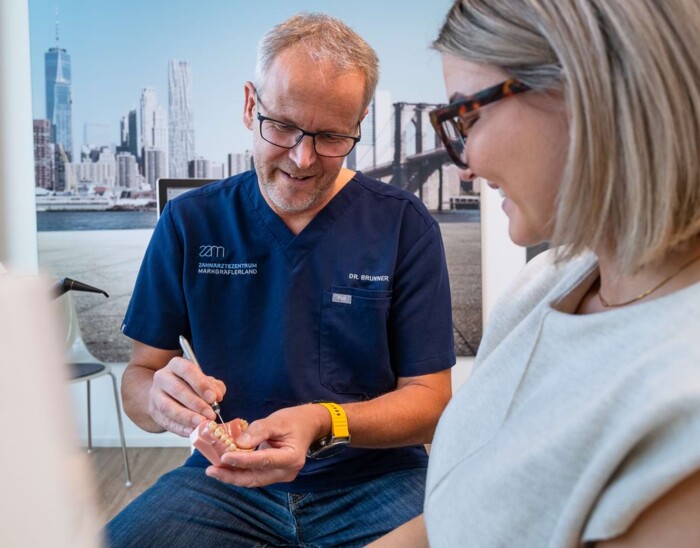 Dr. Brunner zeigt einer Patientin etwas an einem Zahnmodell.